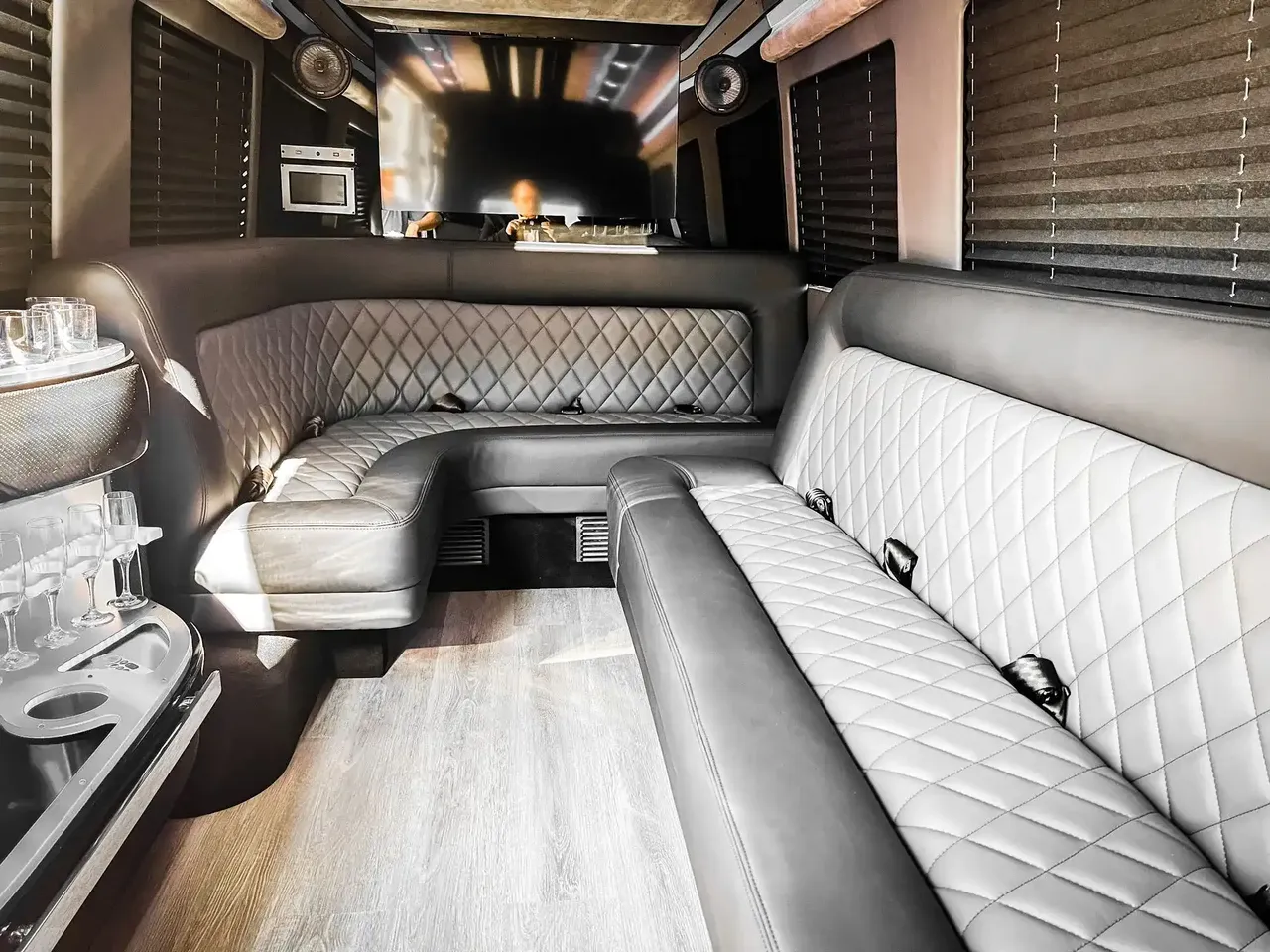Mercedes-Benz Sprinter Limousine interior with perimeter lounge seating, window shades and wood-look flooring for party bus rental in Bedford, TX